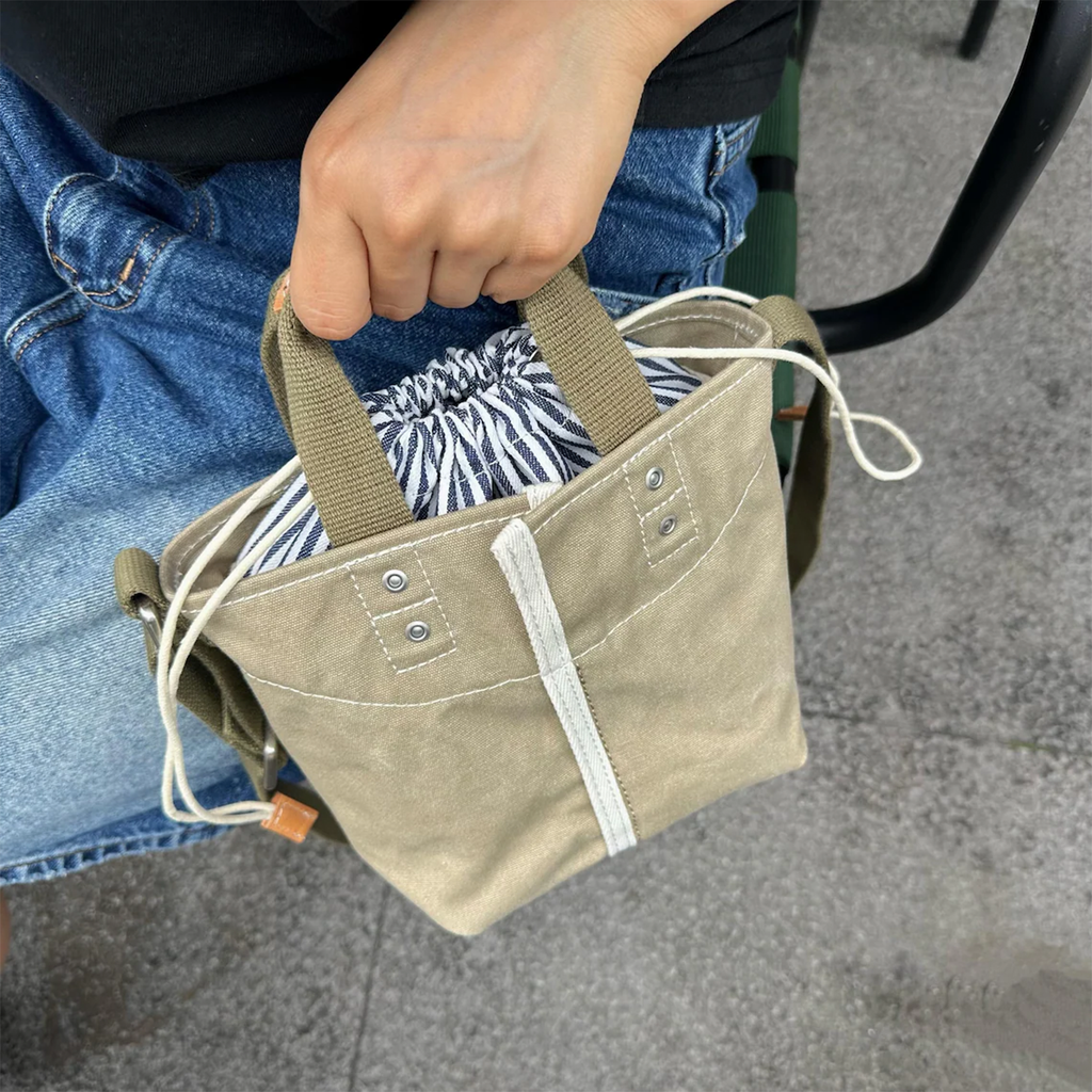 Muted Khaki Woven Mini Bucket Pouch With White Contrast Stitching, Drawstring Striped Liner And Woven Top Hand Loops